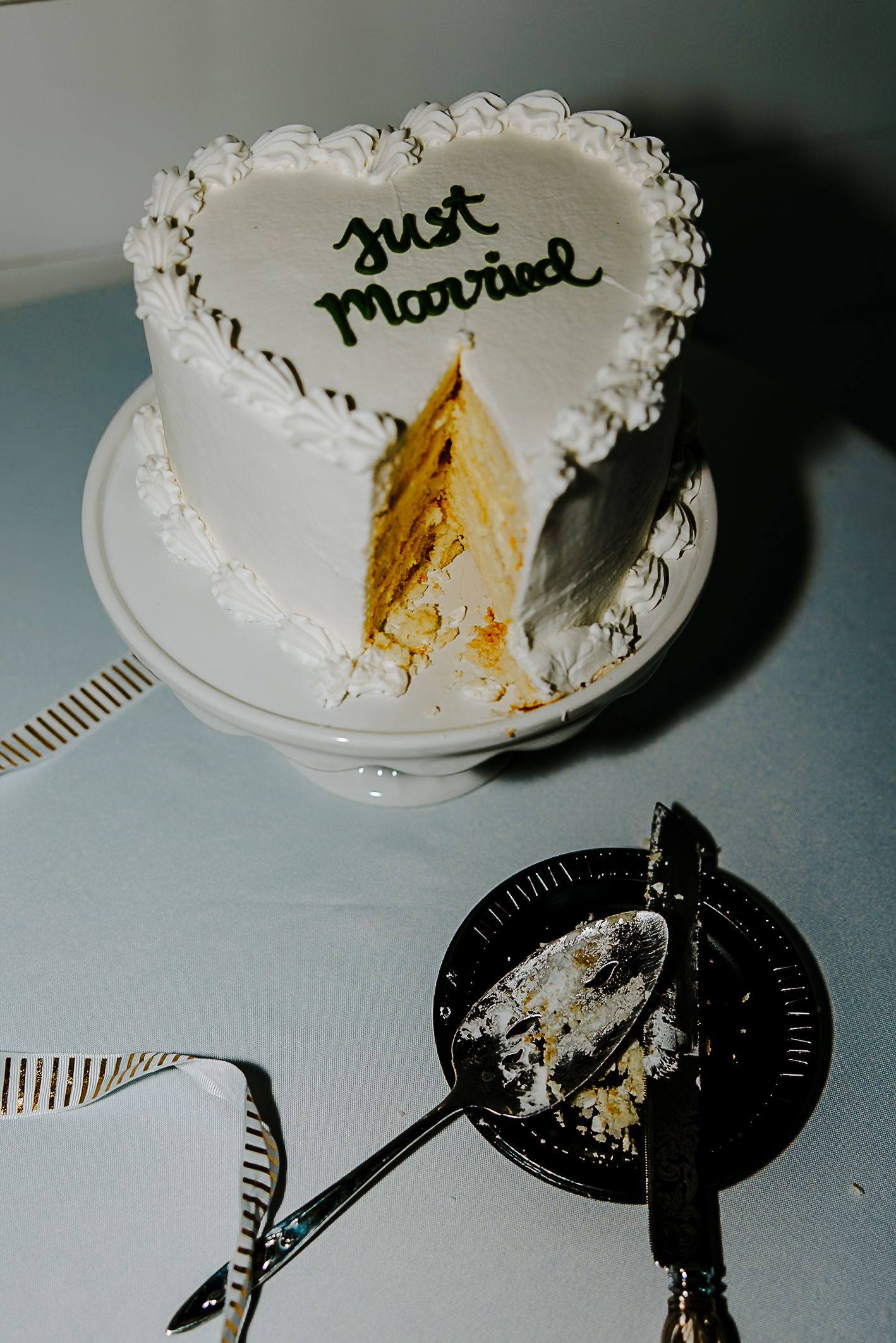 Heart-shaped Just Married wedding cake with a slice removed on a white cake stand.