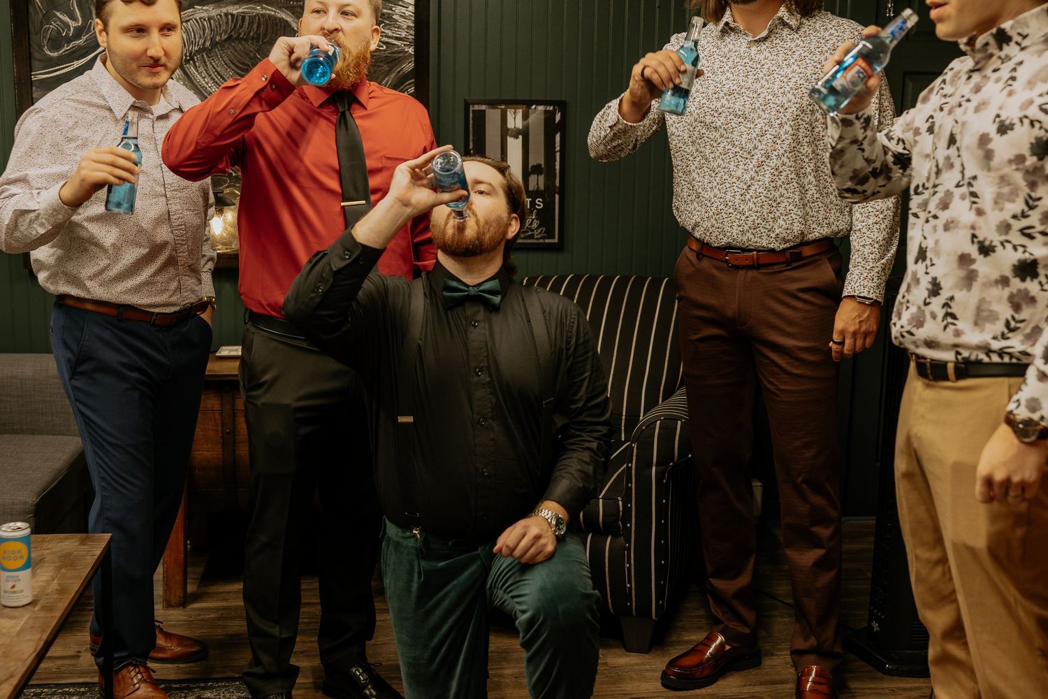 Group of men in dress shirts taking shots at a celebratory indoor party event.