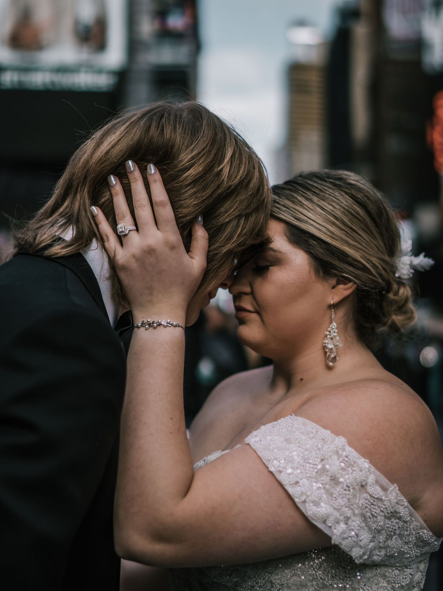 Close-up of bride and groom forehead to forehead, bride showing engagement ring in Times Square NYC.