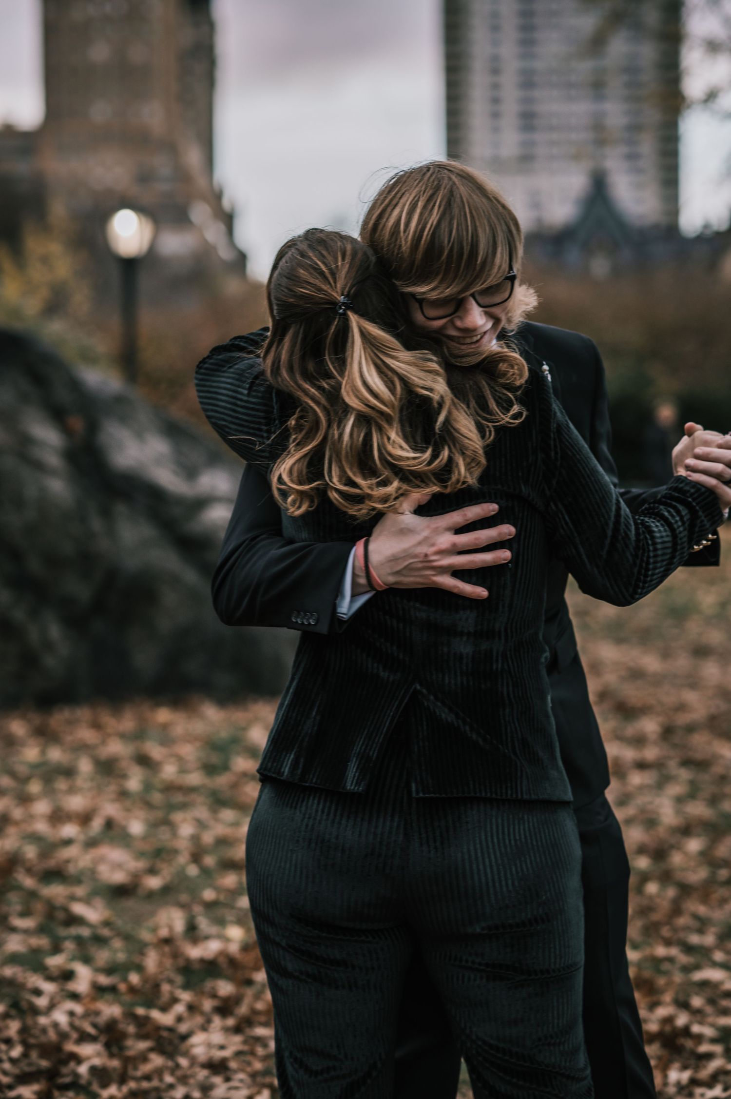 Two guests share a warm hug at an outdoor autumn wedding celebration in Central Park, New York.