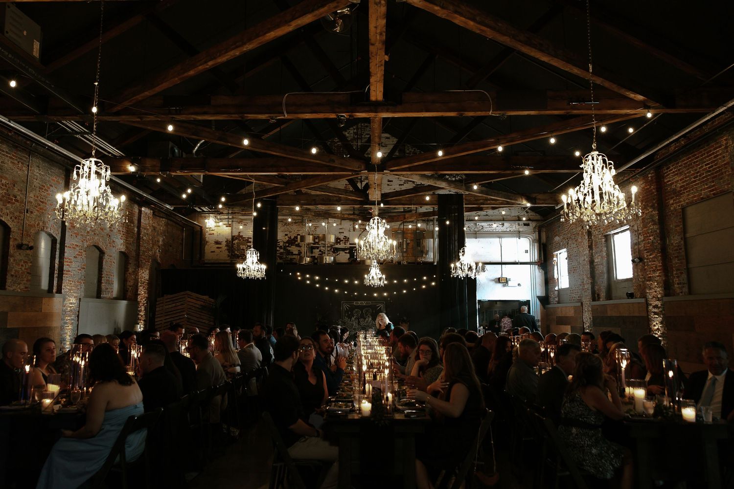 Dimly lit wedding reception hall with string lights, chandeliers, and guests dining.