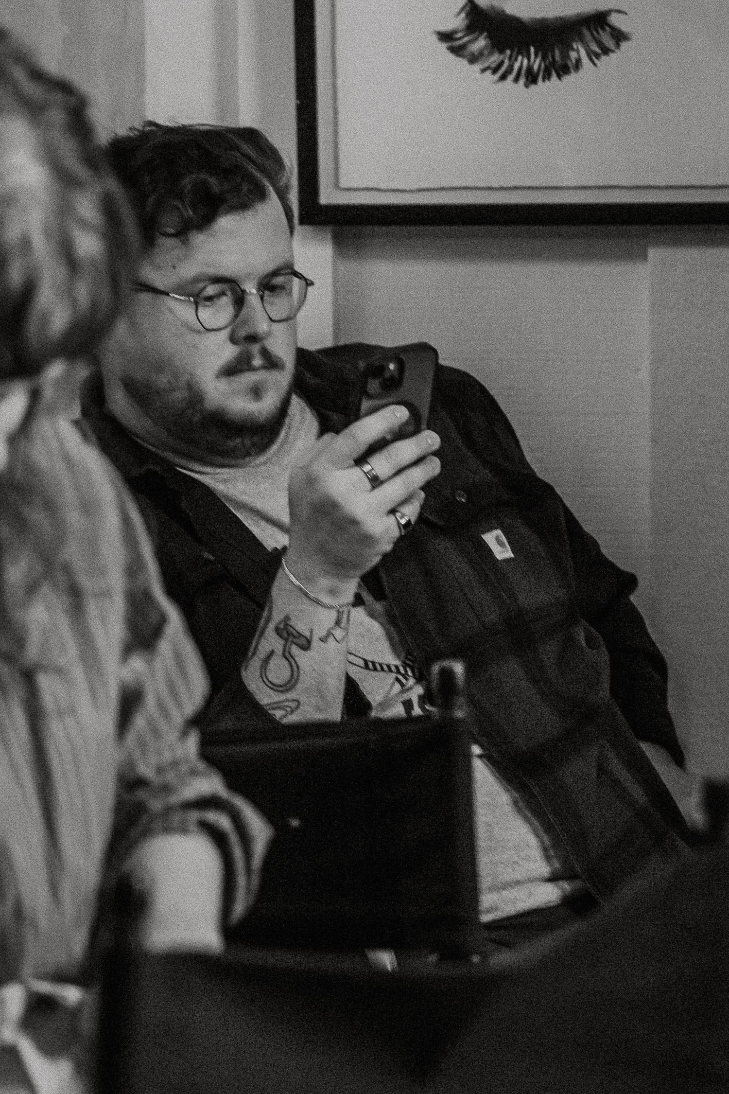 Young man in glasses looking at phone during wedding preparations in black and white.