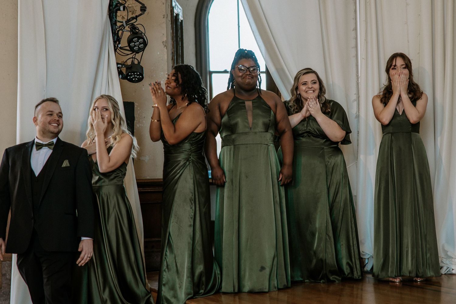 Emotional bridesmaids in olive green satin gowns react with joy at a wedding ceremony at Urban Artifact in Cincinnati, Ohio