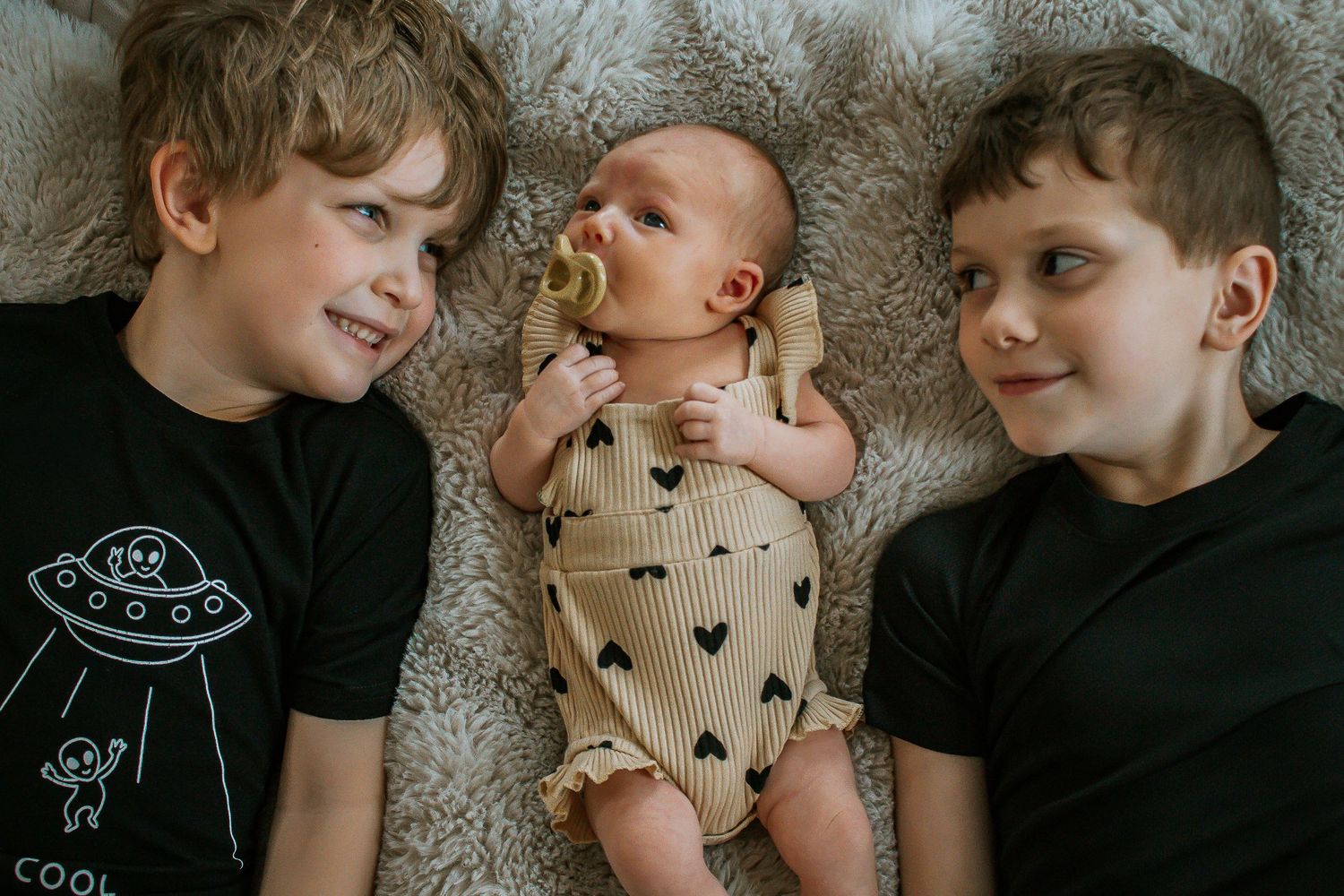 Two older brothers smiling at newborn baby sibling on blanket in Cincinnati, Ohio.