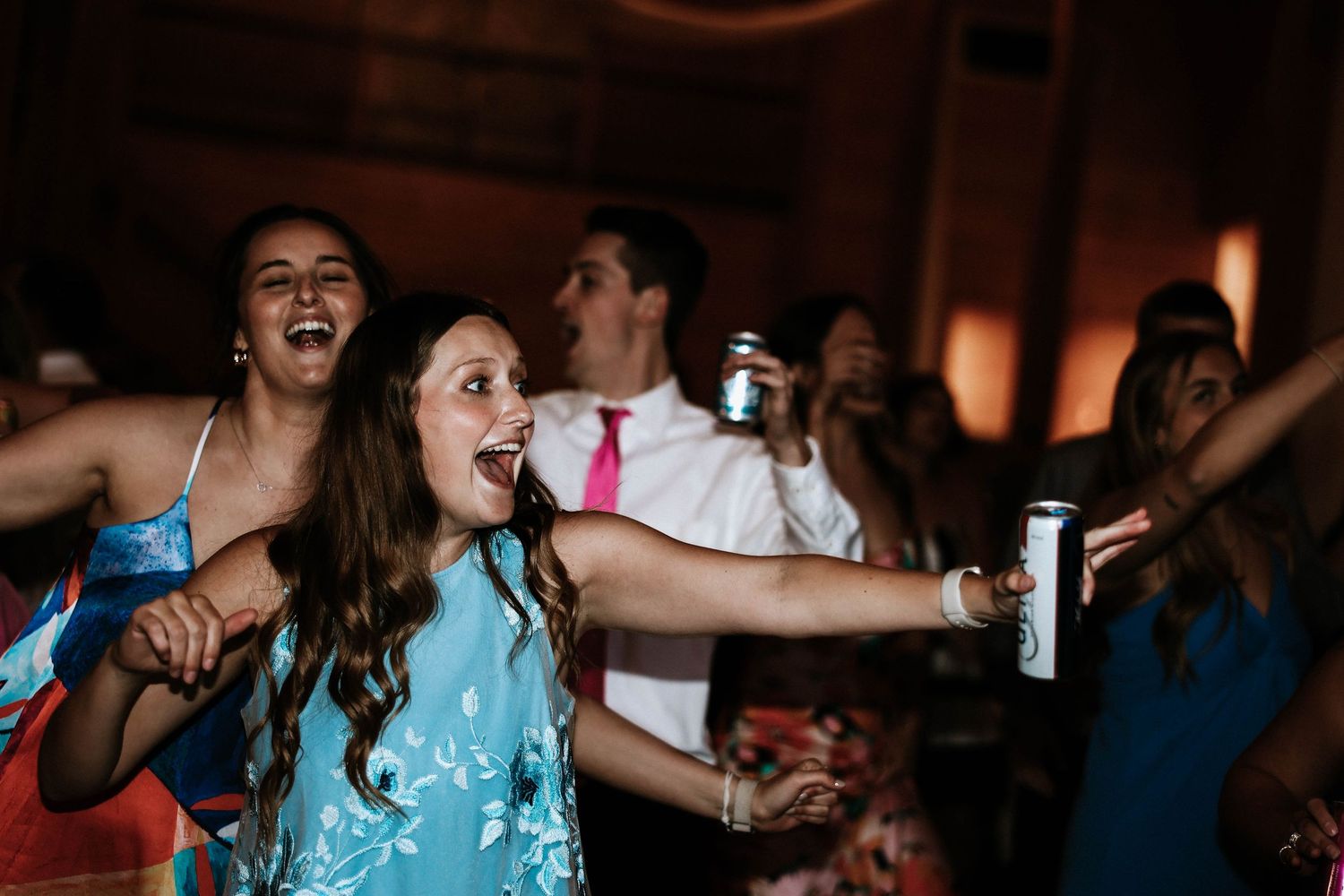 Guests dancing and laughing at a wedding reception, holding drinks and celebrating on the dance floor.