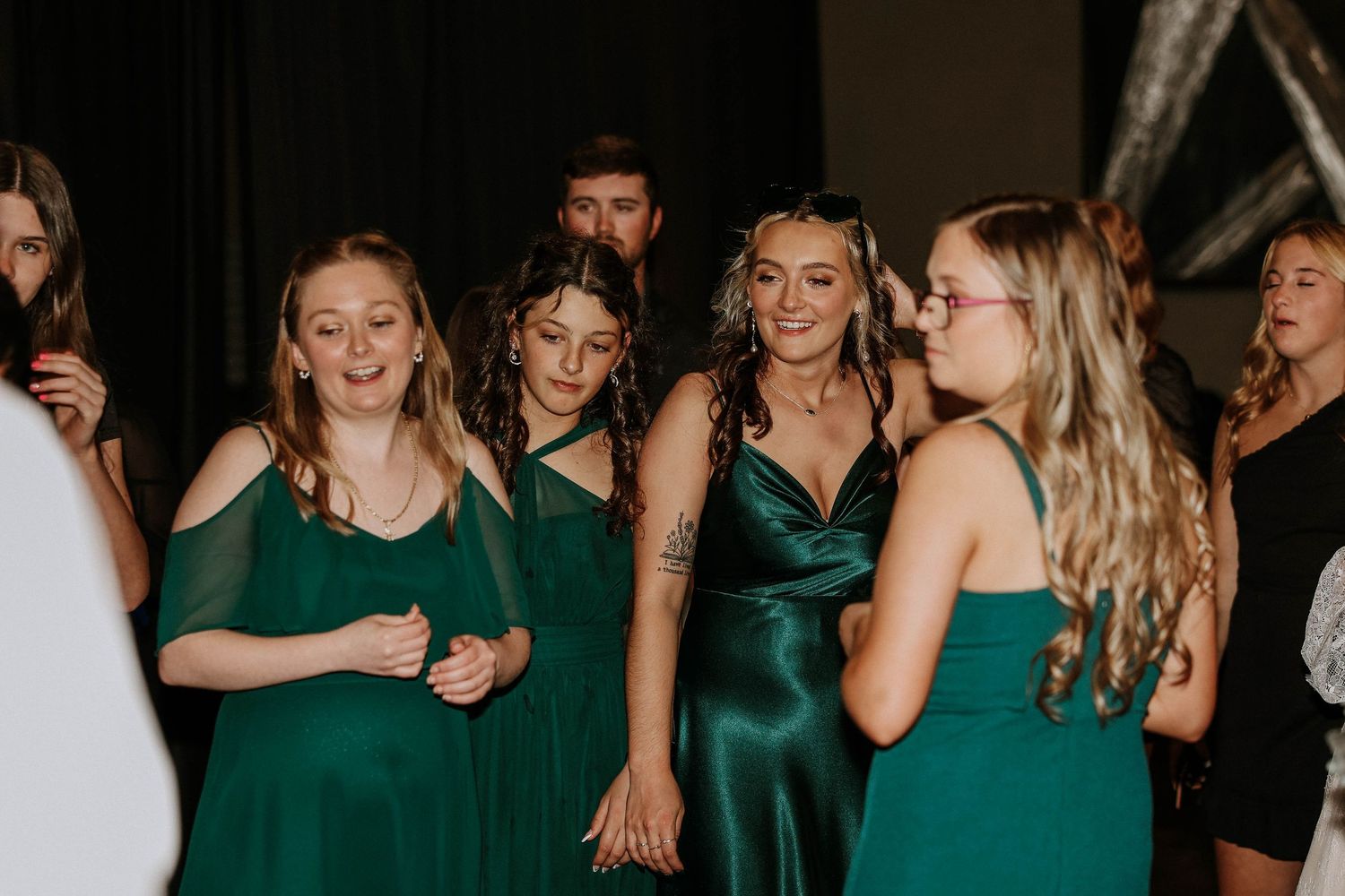 Group of young women in elegant green dresses socializing at a formal event or prom.