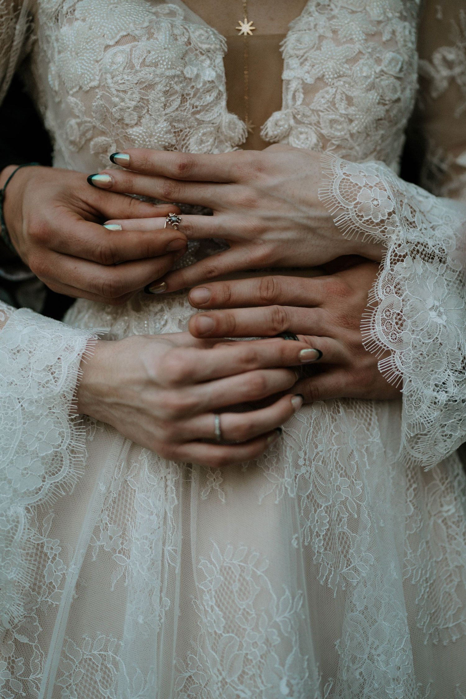 Close-up of couple's hands with rings embracing, bride wearing elegant white lace wedding dress.
