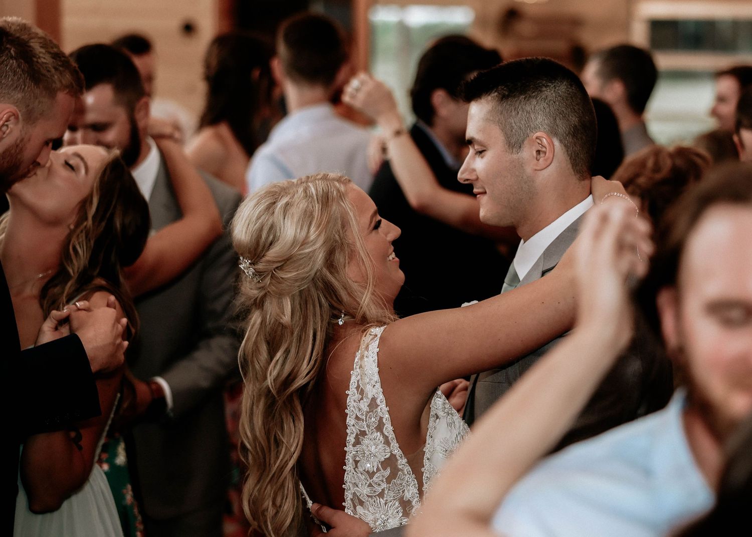Bride and groom share romantic first dance surrounded by guests at rustic barn wedding reception.
