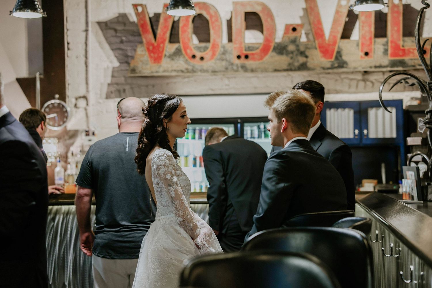 Bride in lace gown stands at a bar with guests at a VOD-VIL venue wedding reception.