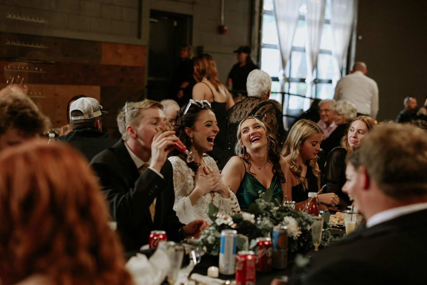 Wedding reception guests sharing joyful moments and laughter at a long decorated dinner table.