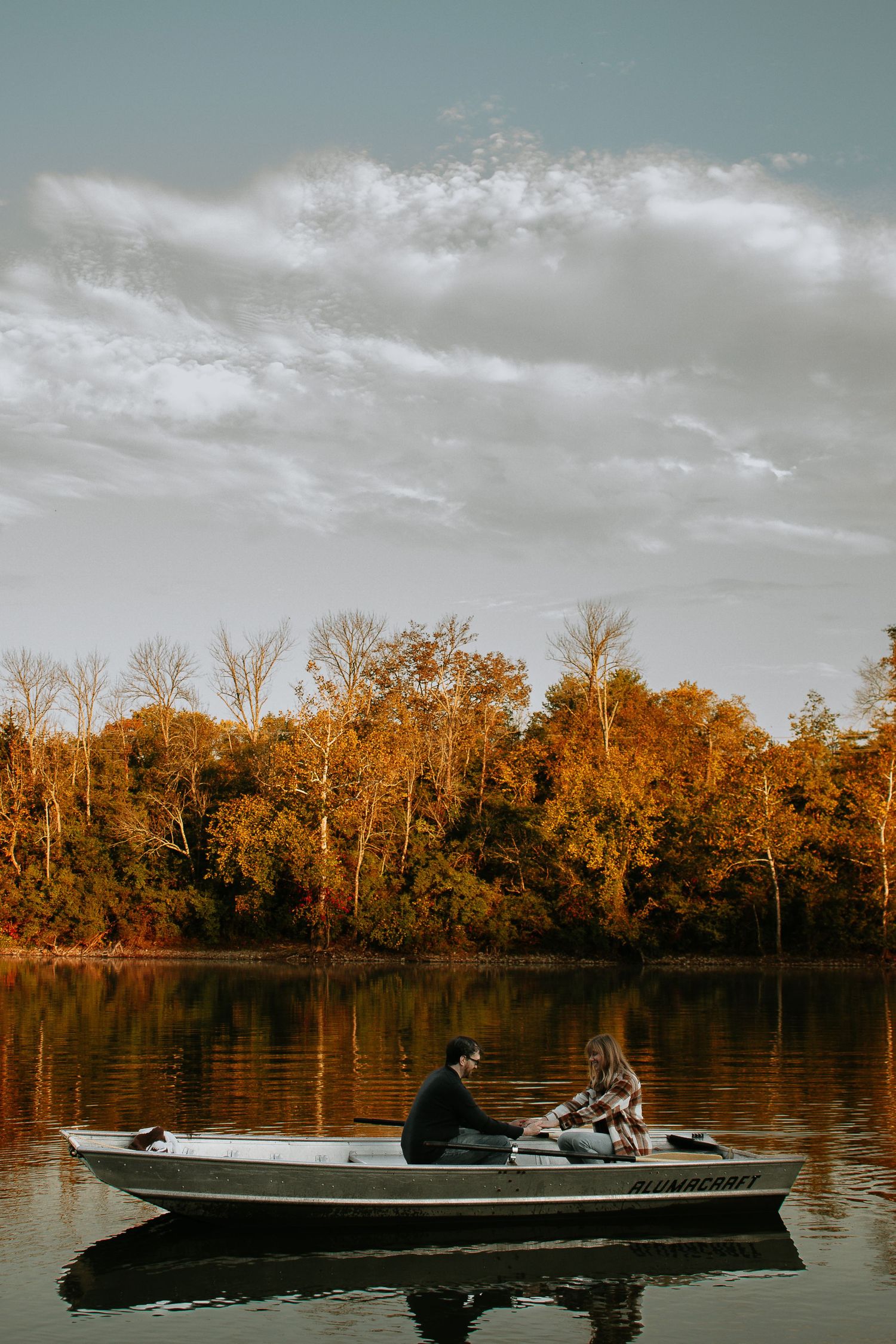 Couple sitting in a small rowboat on a calm lake surrounded by colorful autumn foliage at Winton Woods in Cincinnati, Ohio