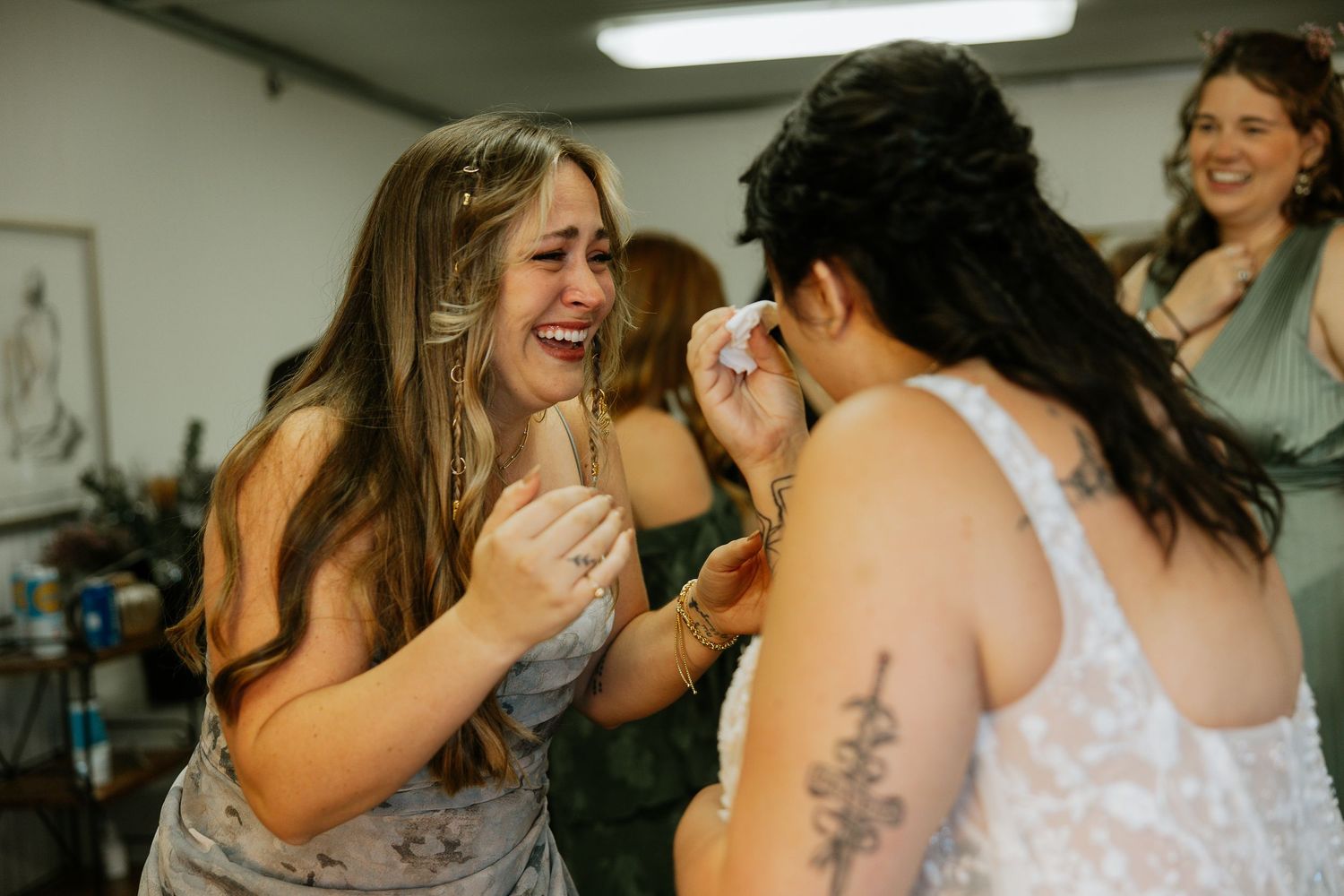 Bridesmaid laughing joyfully while helping bride with makeup during wedding preparations.