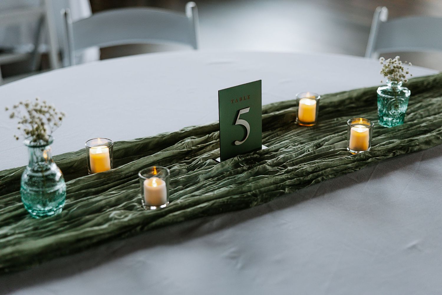 Wedding table centerpiece with table number 5, candles, and small floral bud vases.