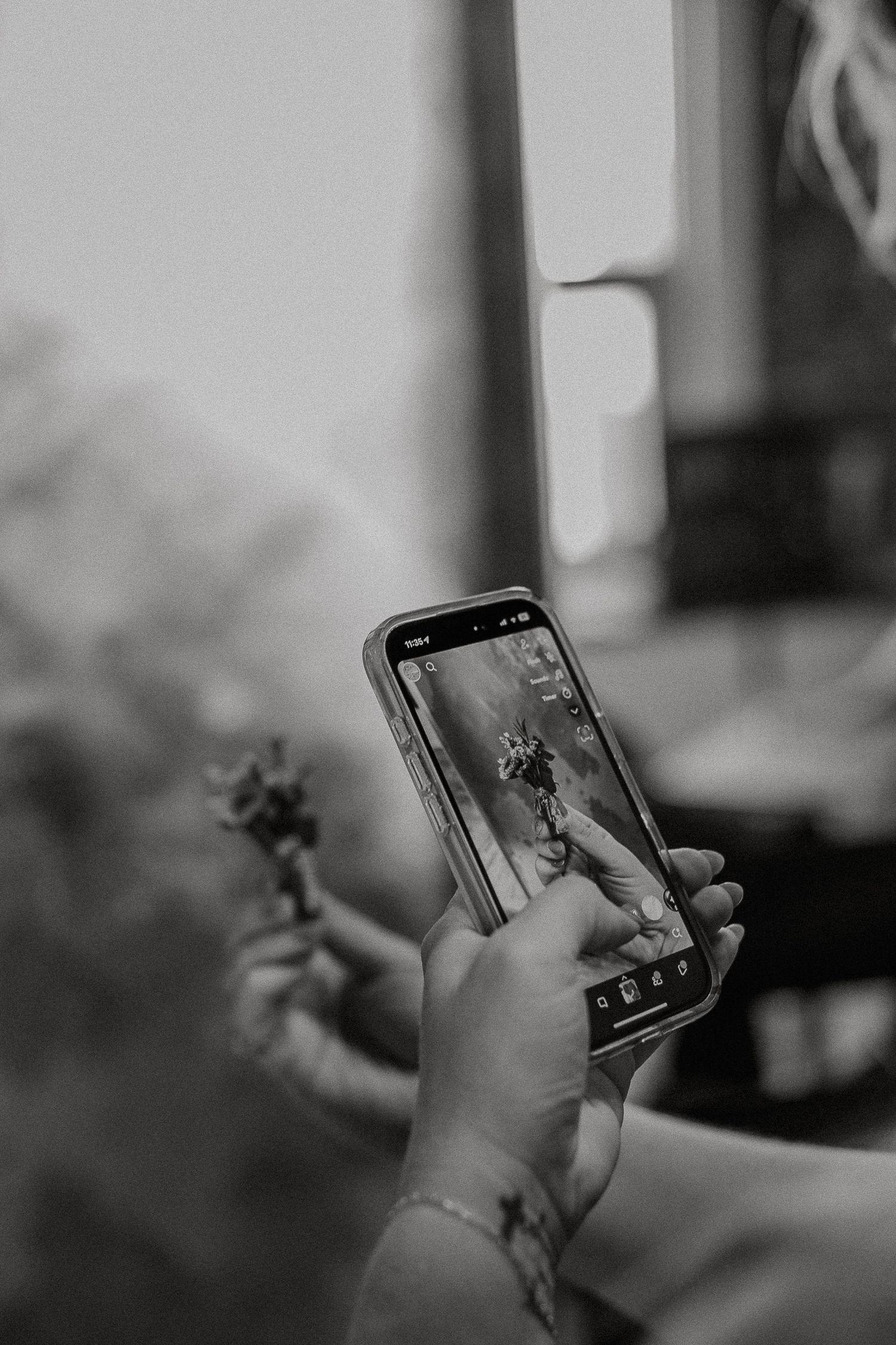 Close-up black and white photo of hands holding a smartphone photographing flowers.