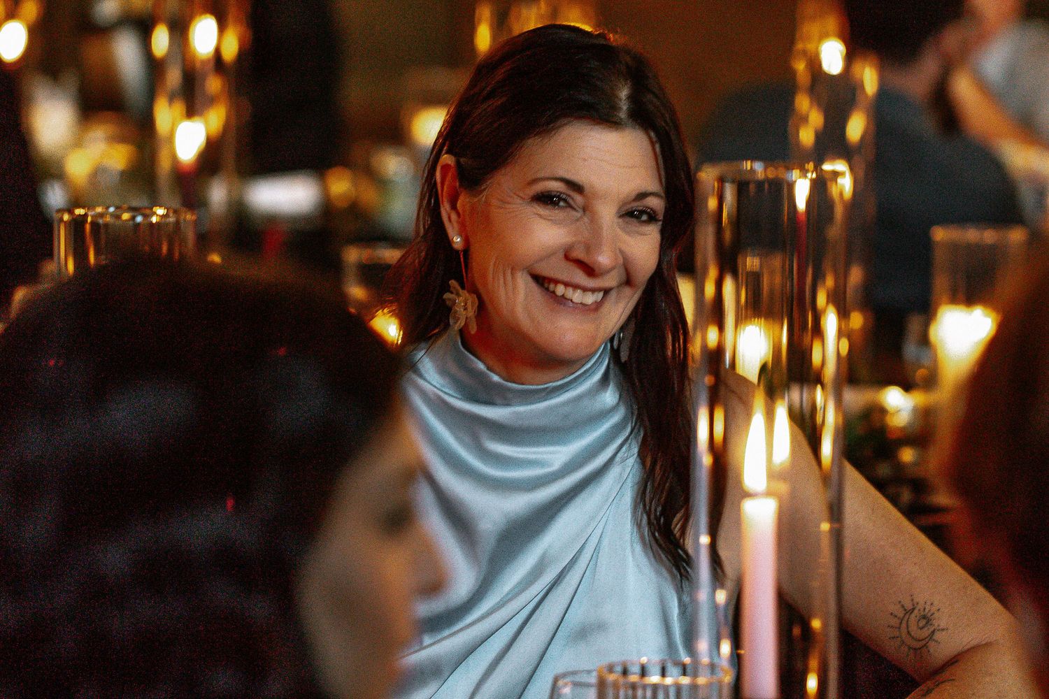 Elegant woman in blue dress smiling warmly at candlelit wedding reception table.