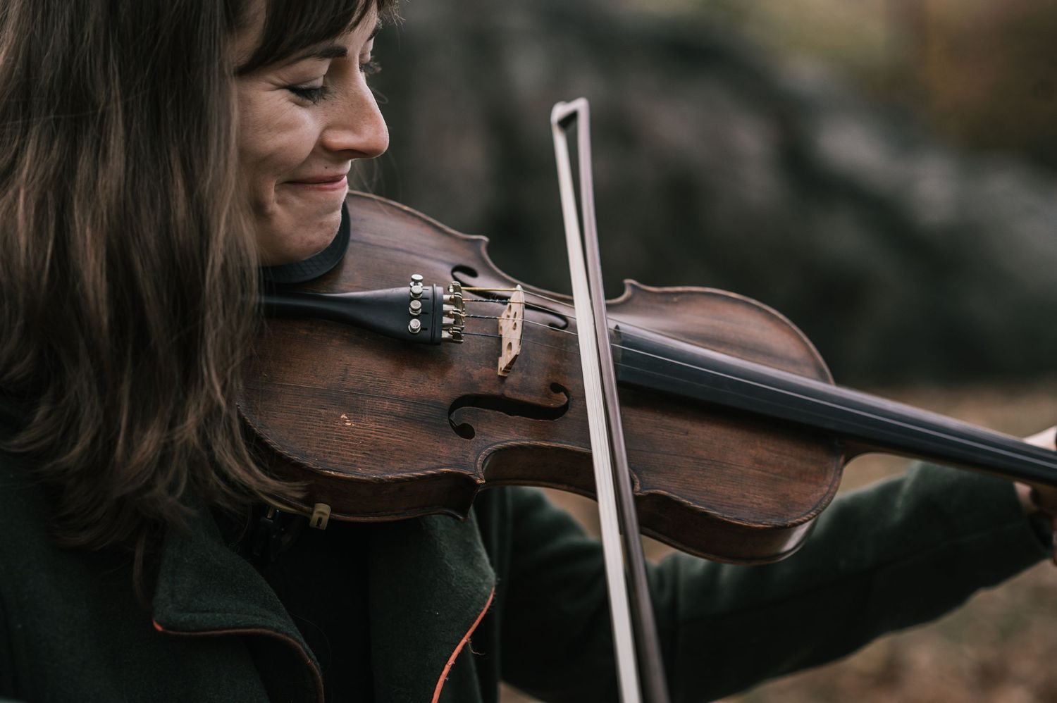 Smiling female violinist playing classical music outdoors at a wedding ceremony in natural setting.