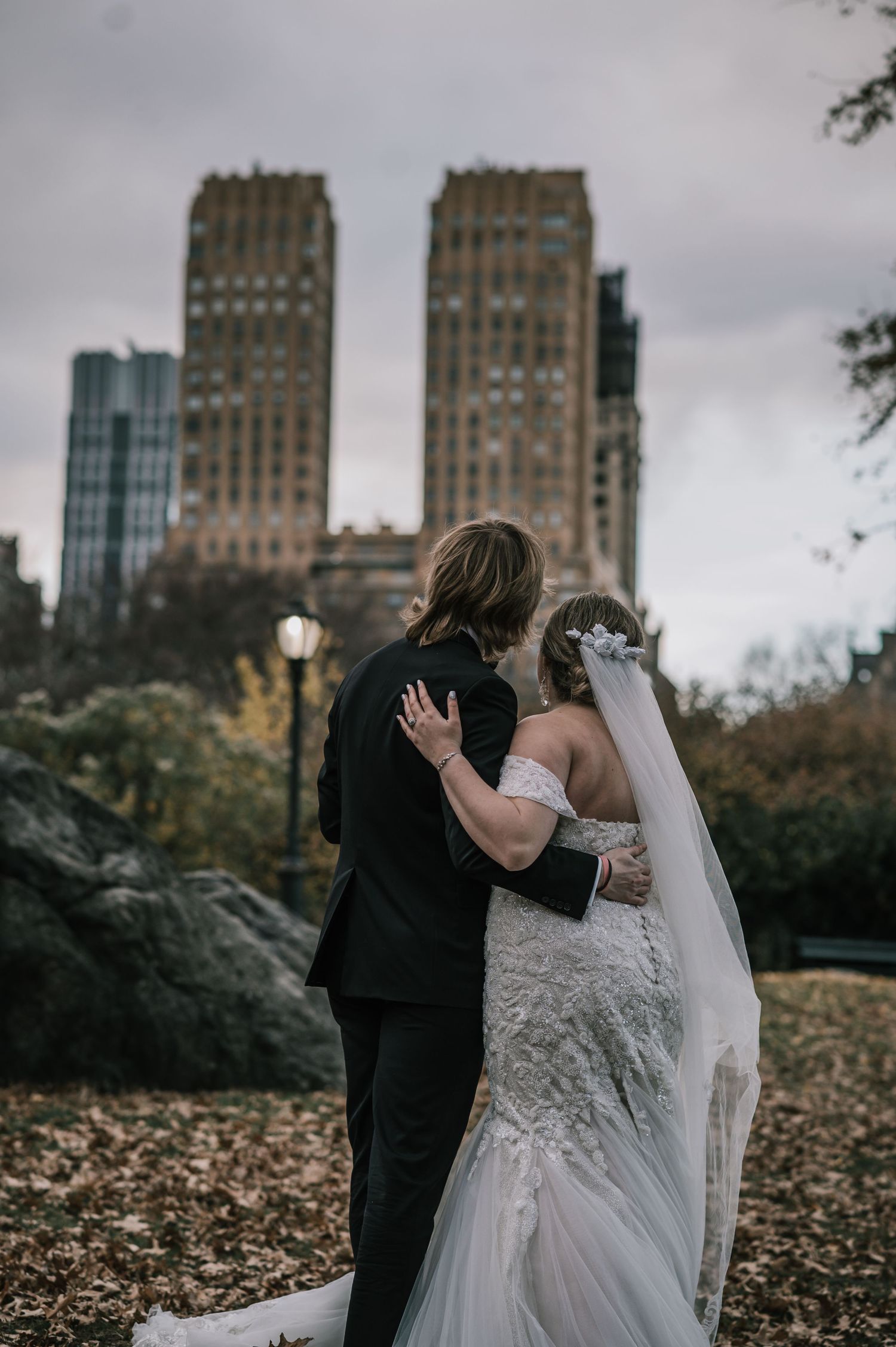 Bride and groom embrace in Central Park with NYC skyline in background during autumn wedding photo session.