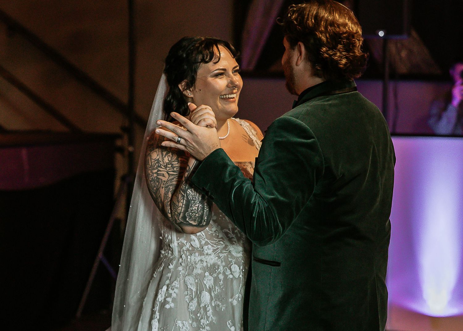 Groom in green velvet suit tenderly touching bride's face during first dance.