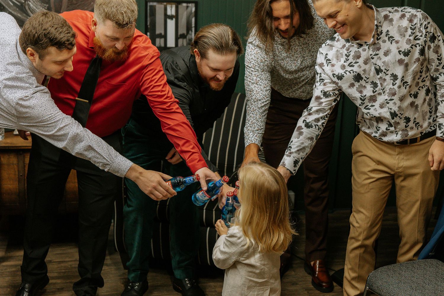 Group of men in formal attire interacting with a young blonde child at an indoor gathering.