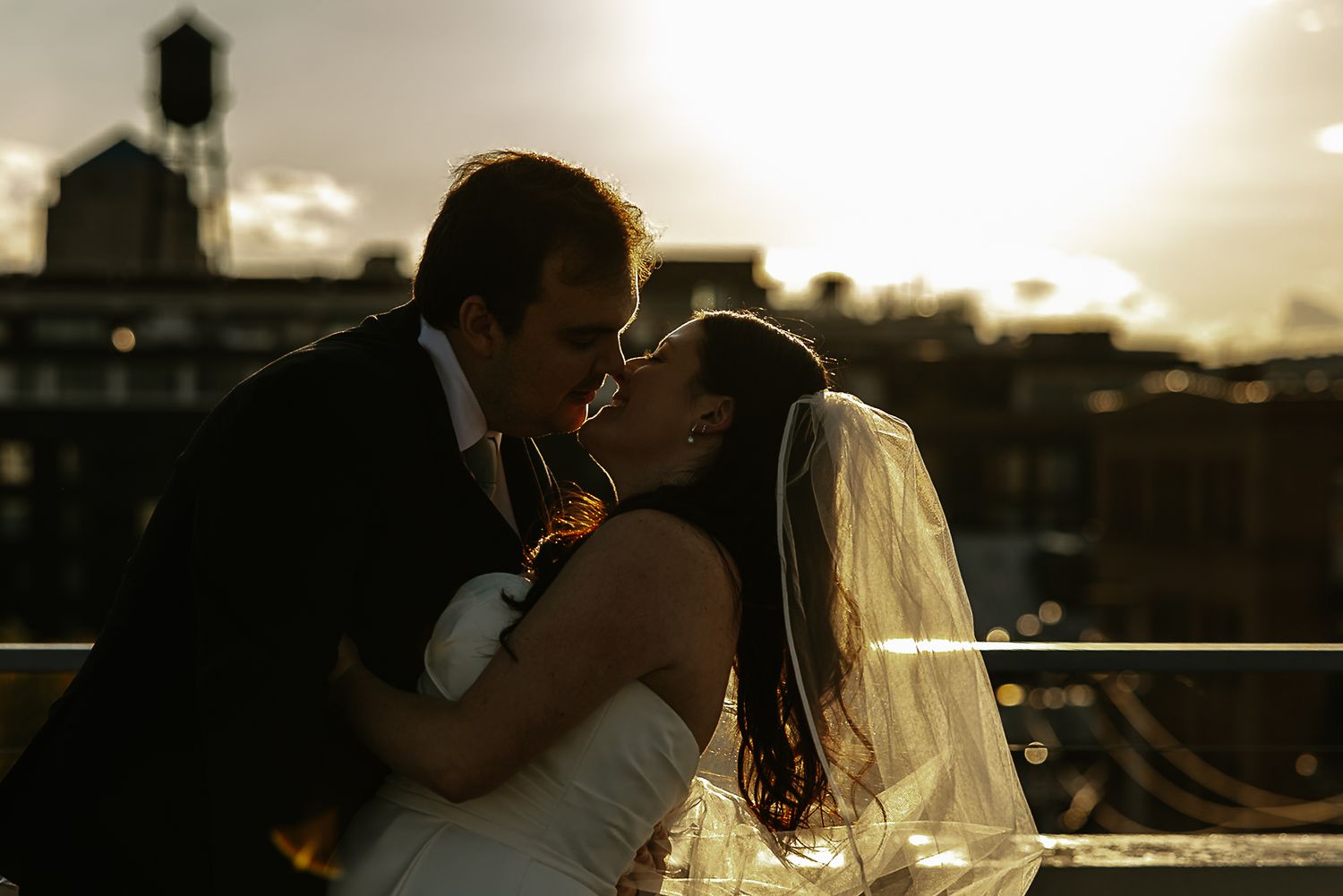 Bride and groom share a romantic rooftop kiss at sunset with a city skyline in the background at The Remedy in Dayton, Ohio