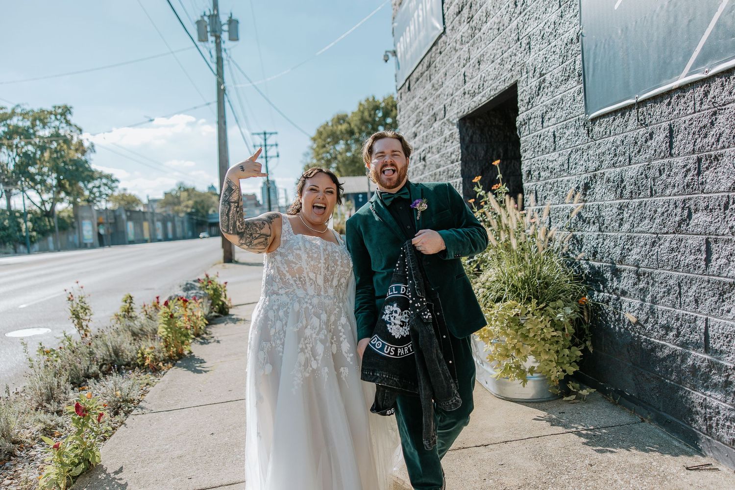 Laughing bride and groom in green suit walk together outside on sunny wedding day near brick building at The Brightside in Dayton, Ohio