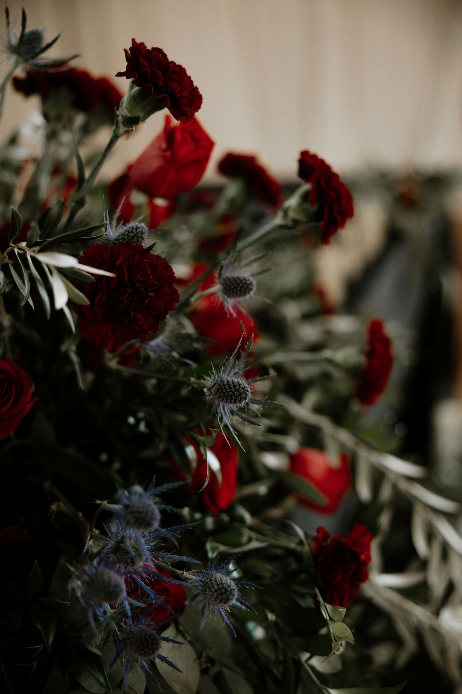Close-up of deep red roses and blue thistle wedding floral arrangement with lush greenery at Urban Artifact in Cincinnati, Ohio