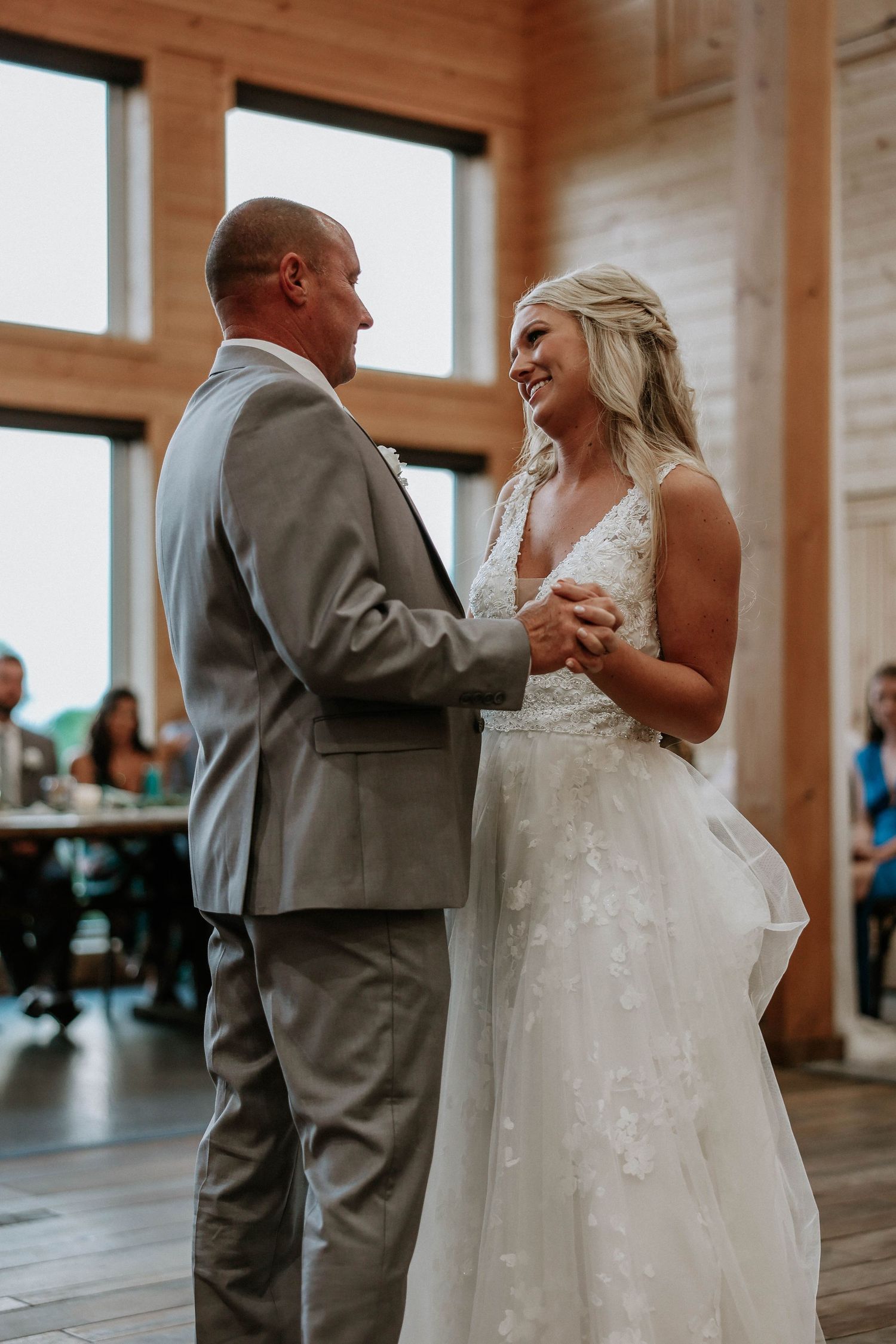 Bride and groom share first dance in rustic barn wedding venue, smiling joyfully at each other.