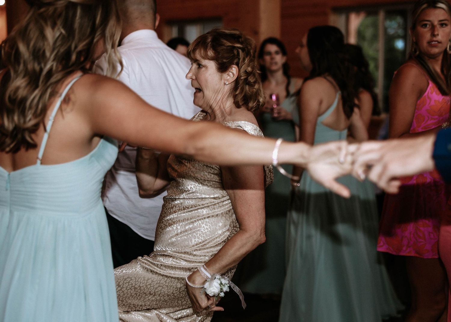 Wedding guests in elegant attire dance and laugh together joyfully at a lively reception celebration.
