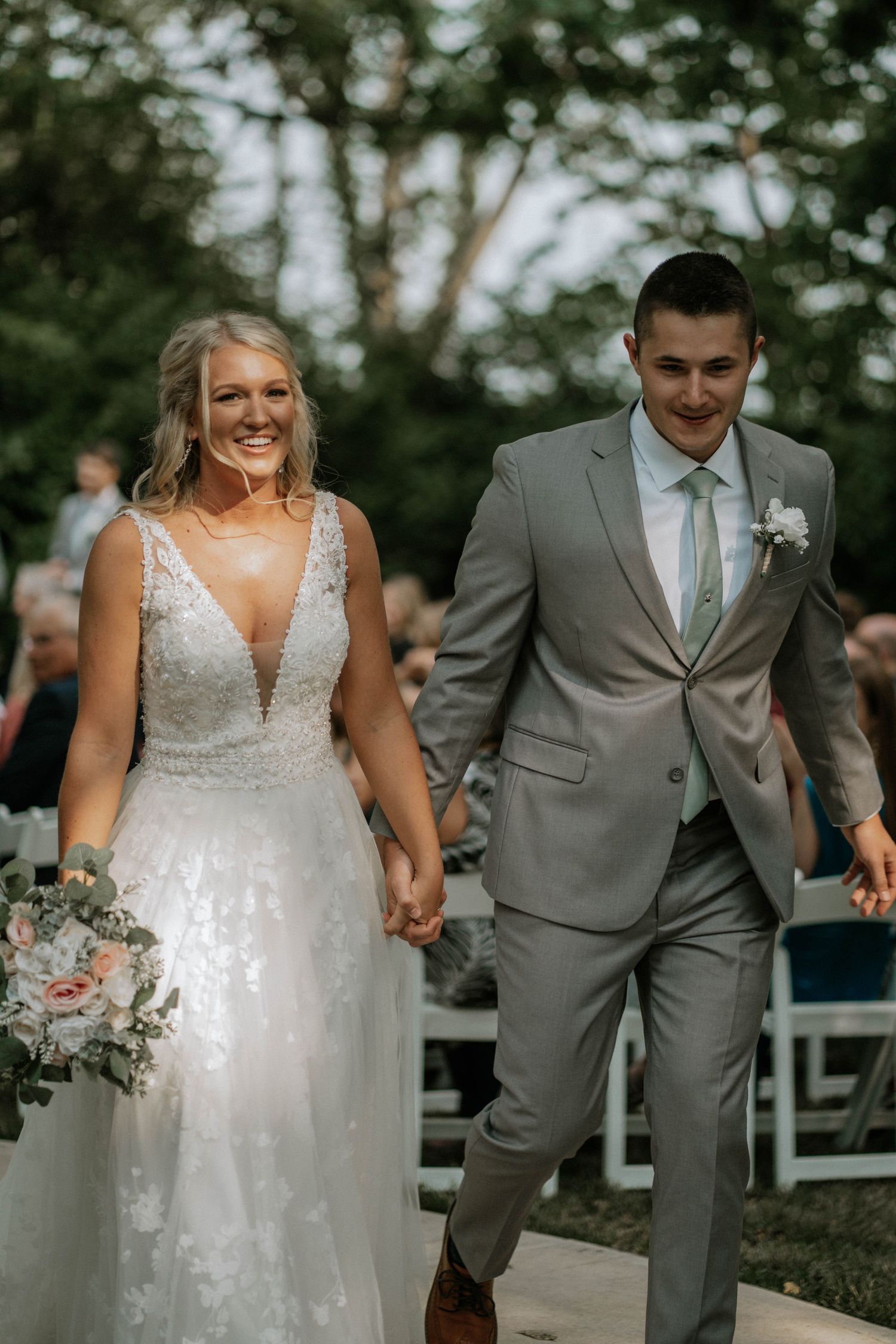 Bride and groom walk down the aisle hand in hand, smiling joyfully, bride holding a pink bouquet.