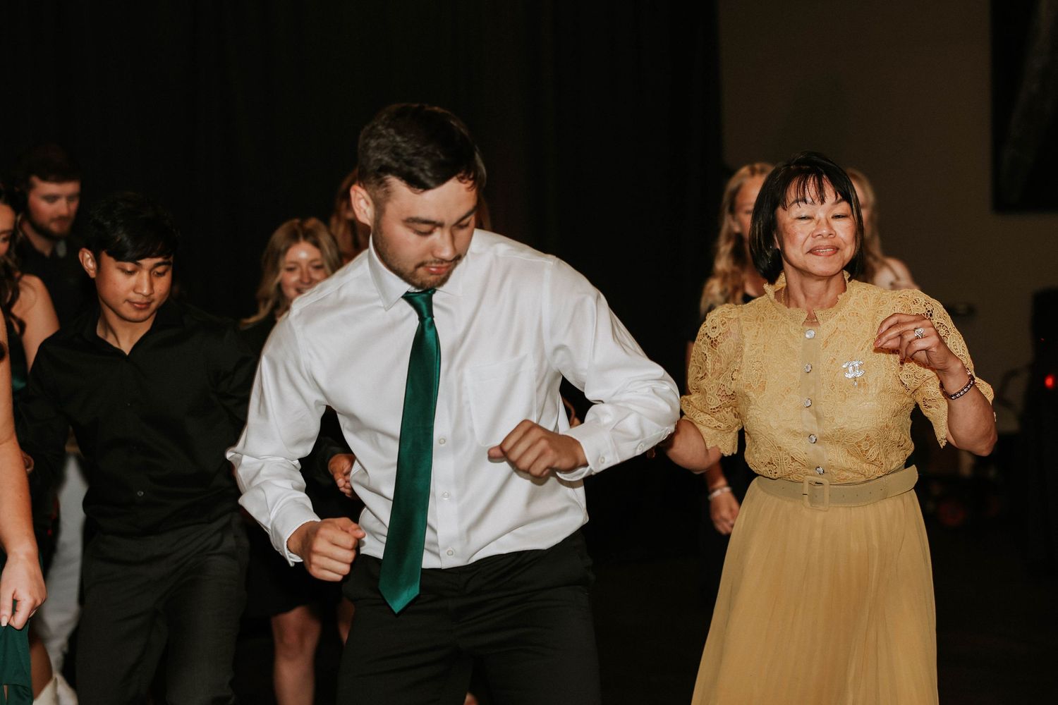 People dancing energetically at a formal event, man in white shirt and green tie with woman in gold blouse.