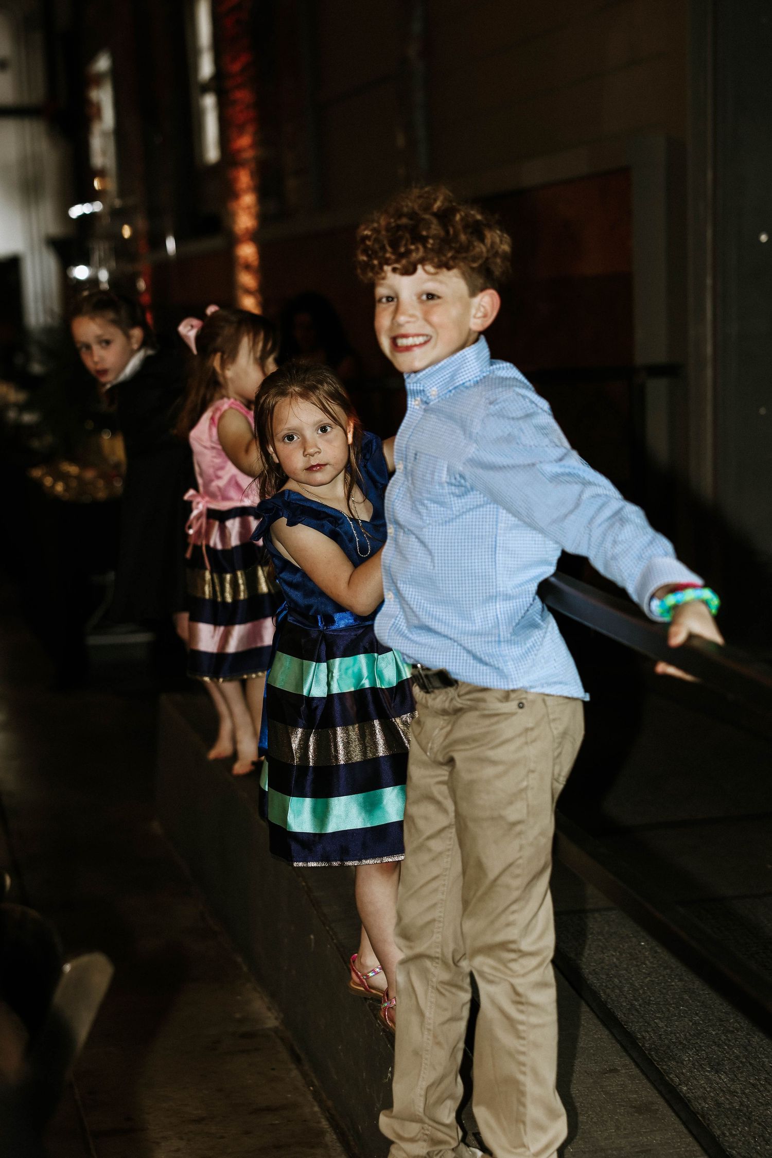 Two children dressed up in formal attire smile and pose together at an indoor event.