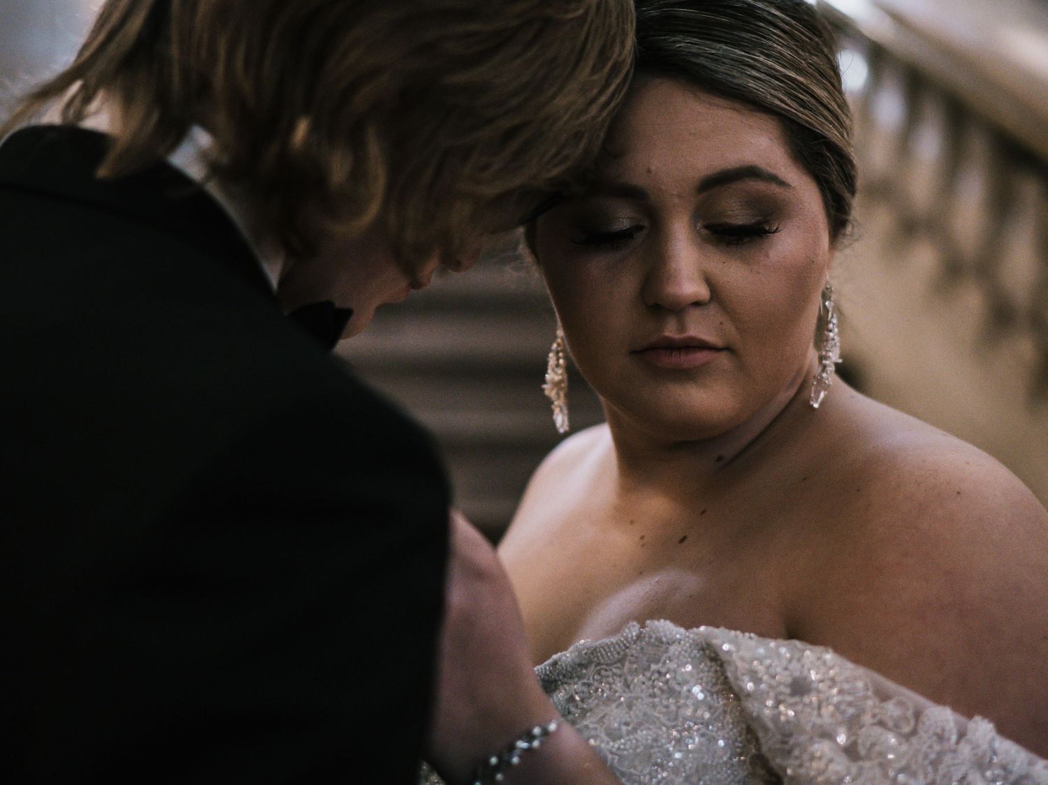 Groom tenderly adjusts bride's beaded off-shoulder wedding gown in a close romantic moment.