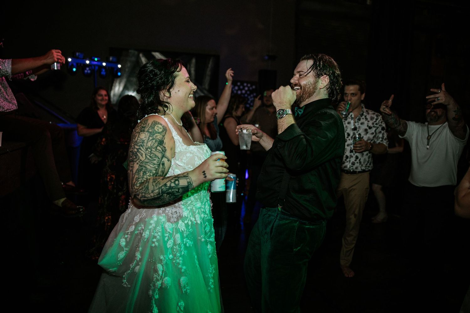 Bride and groom laughing and singing together on a green-lit wedding reception dance floor.
