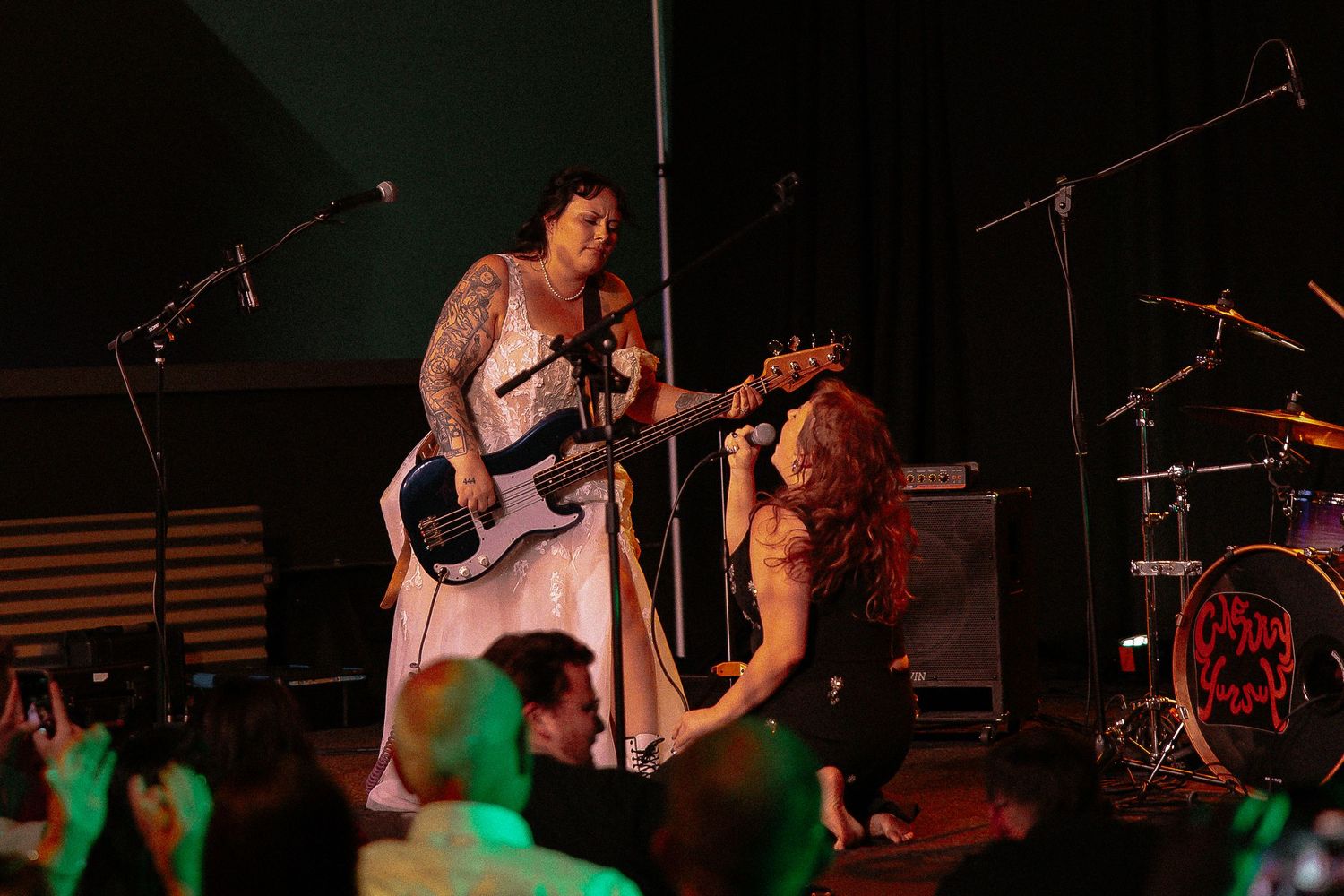 Two female musicians share microphone moment on stage at live wedding reception concert.
