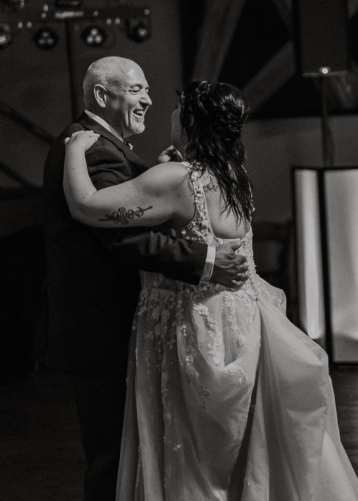 Black and white photo of a smiling bald man dancing with a bride in a wedding gown.