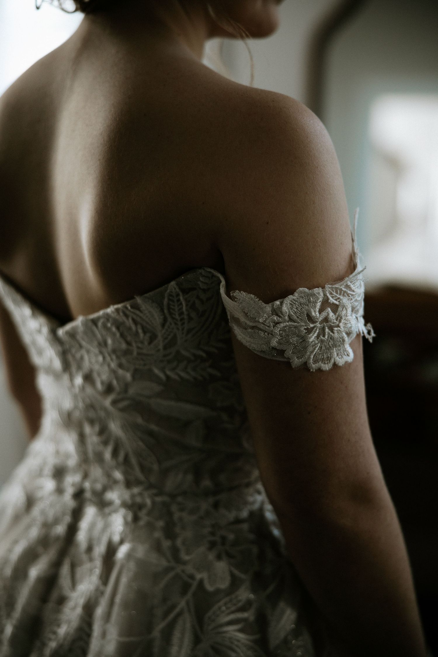 Close-up back view of bride wearing an off-shoulder lace wedding gown with floral applique detail at Urban Artifact in Cincinnati, Ohio
