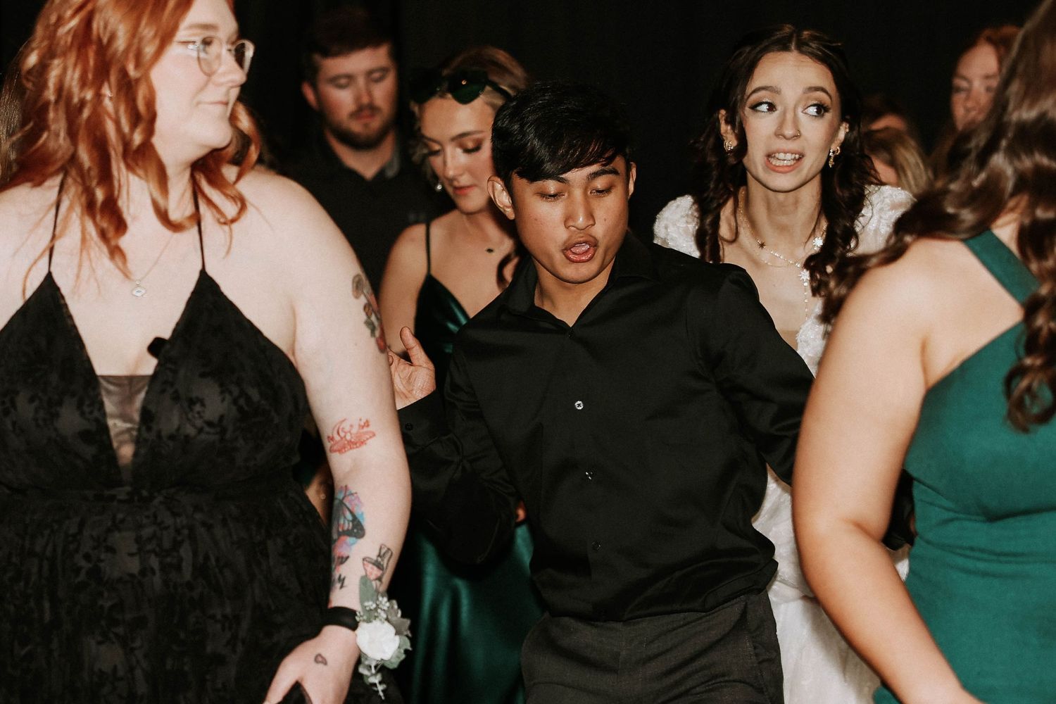 Young adults dancing energetically at a formal event, wearing elegant attire including black and green dresses.