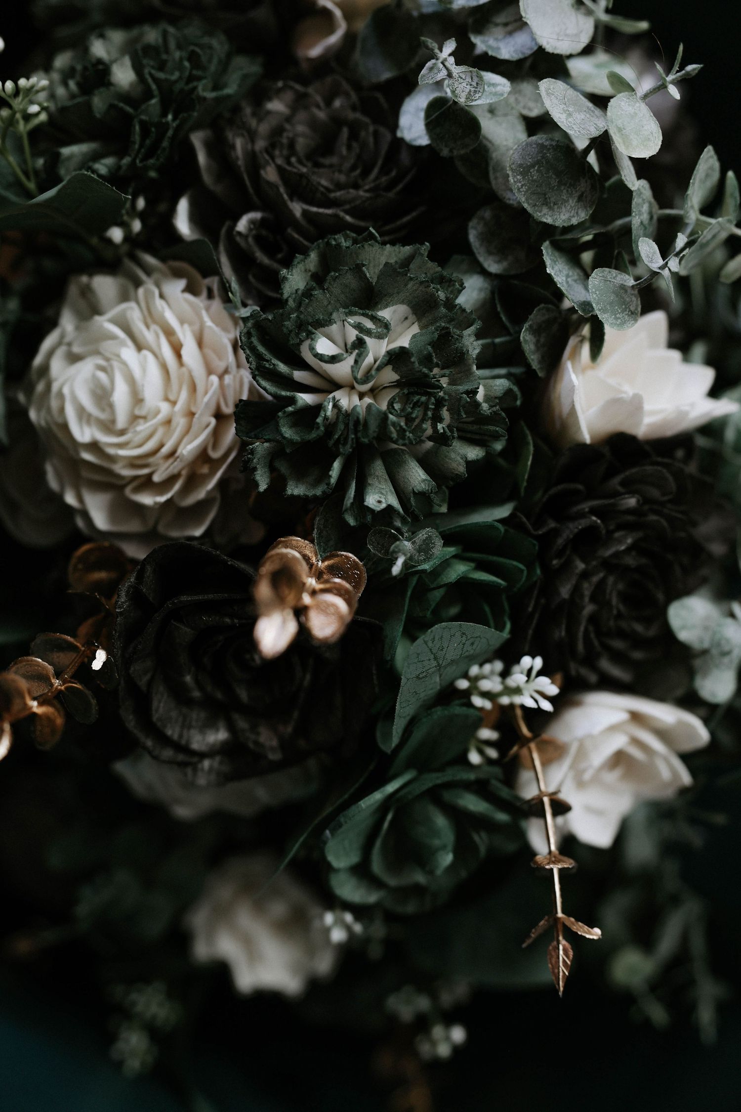Dark moody floral arrangement with white roses, dark blooms, eucalyptus, and gold accents for elegant wedding decor.