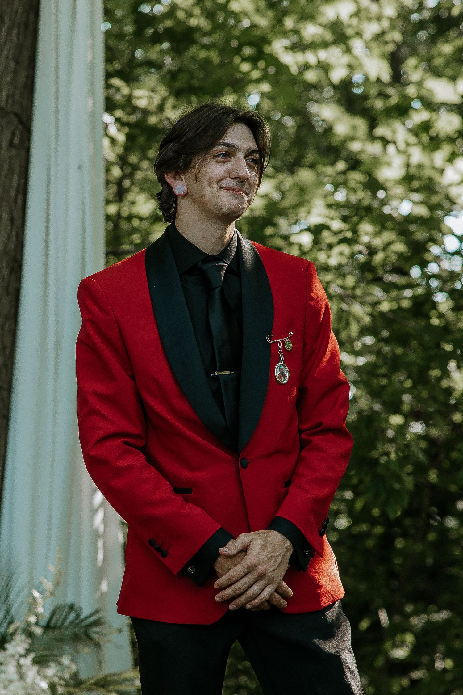Groom smiling in bold red jacket with black lapels standing outdoors at the Bella Amore on Enchanted Acres in Dennison, Ohio