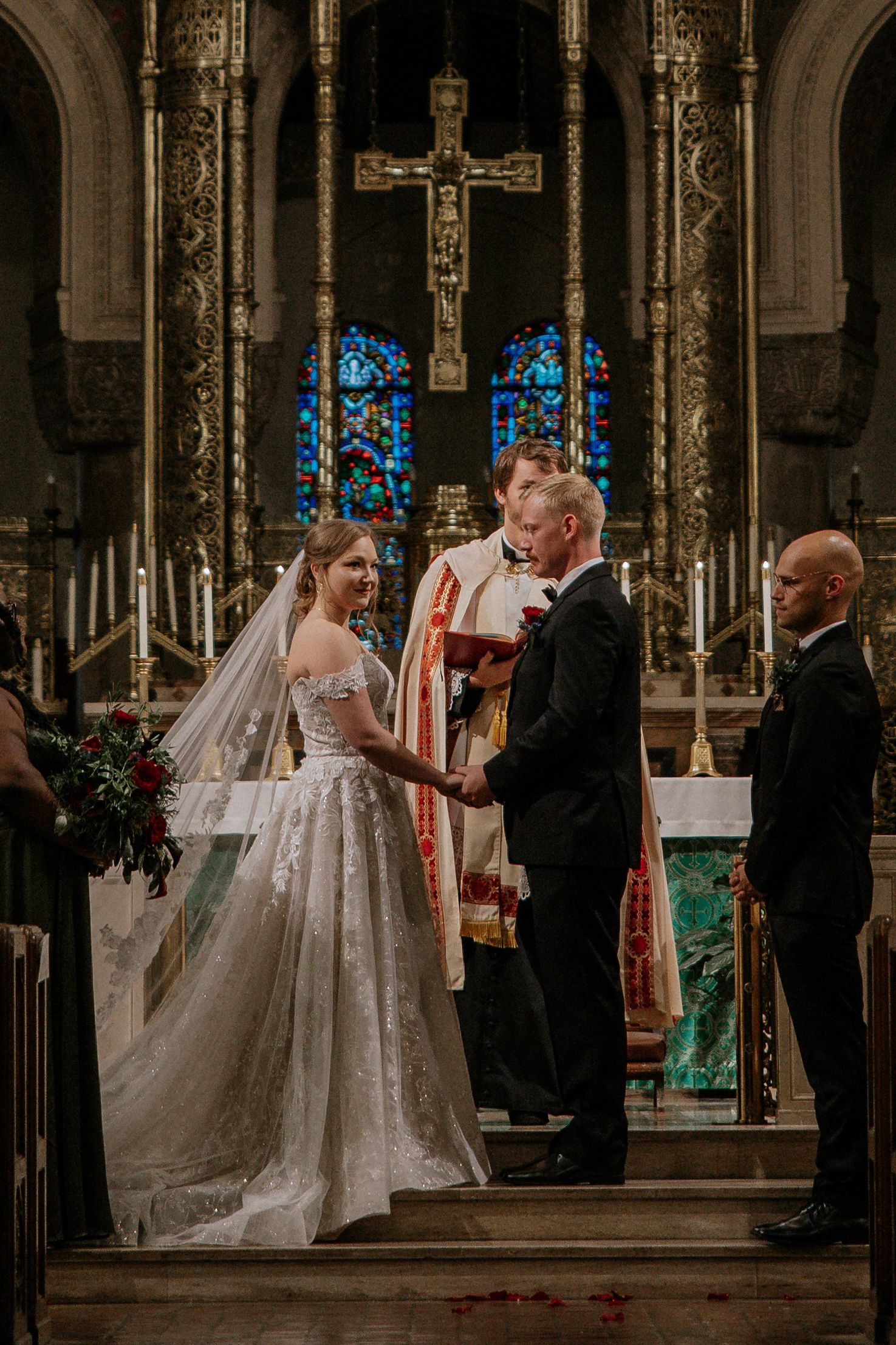 Bride in lace gown and groom hold hands at altar with priest during church ceremony in Cincinnati, Ohio