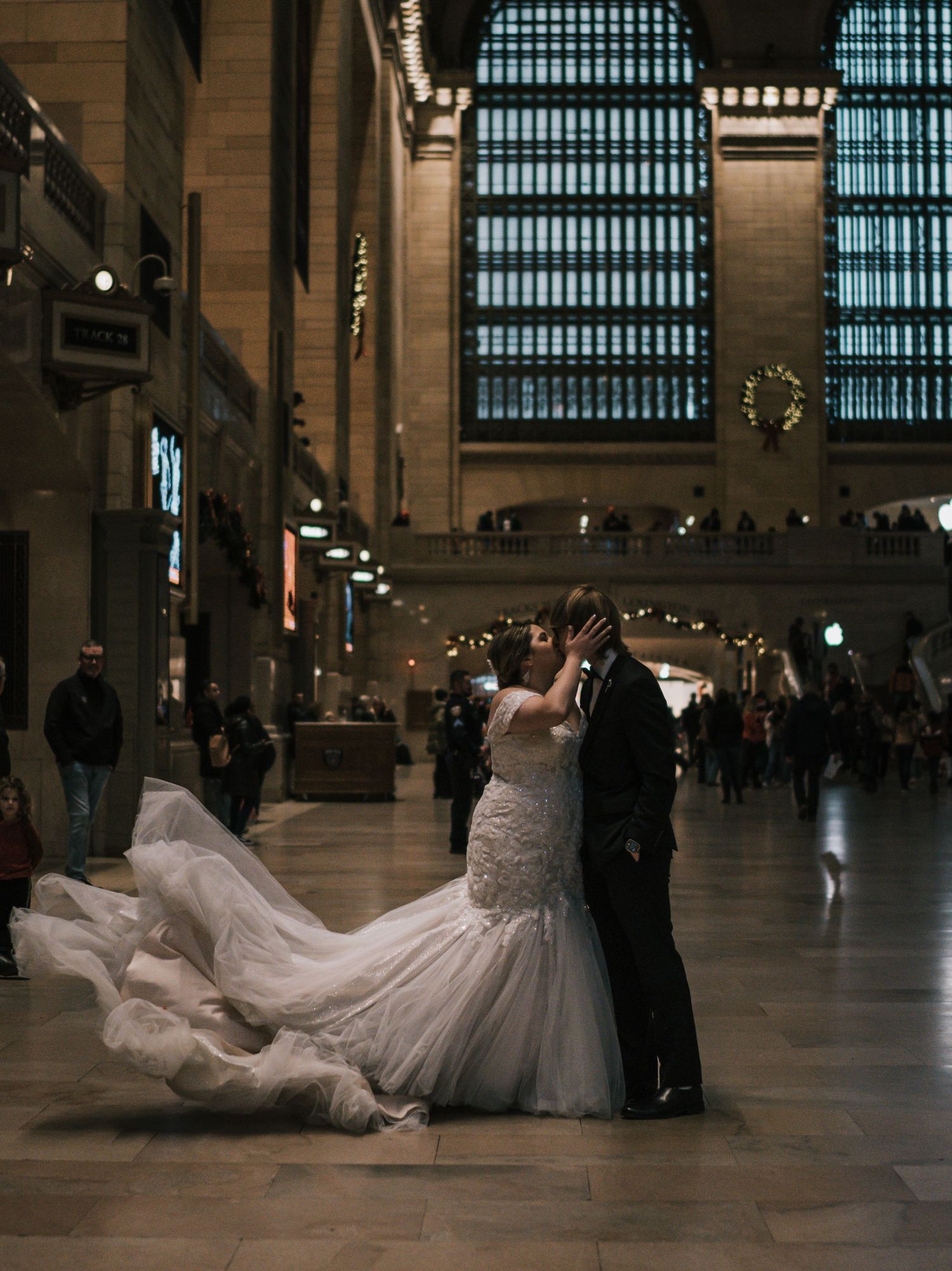 Couple shares romantic kiss at Grand Central Terminal, bride's cathedral veil flowing dramatically.