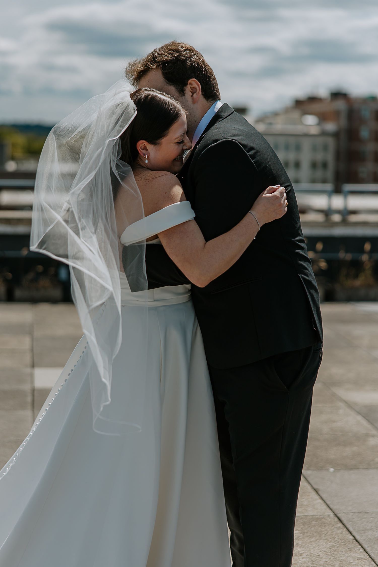 Bride and groom sharing a tender embrace on a rooftop with city skyline in the background.