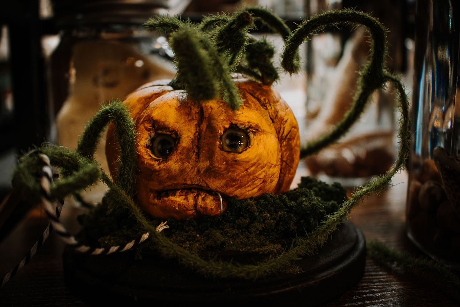 Spooky carved pumpkin decoration with curling green vines on a moss bed, perfect for Halloween display.