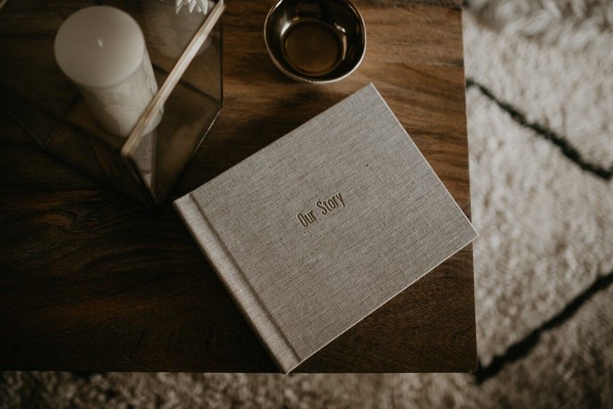 Linen hardcover photo book titled Our Story on a wooden table with candle decor in Cincinnati, Ohio