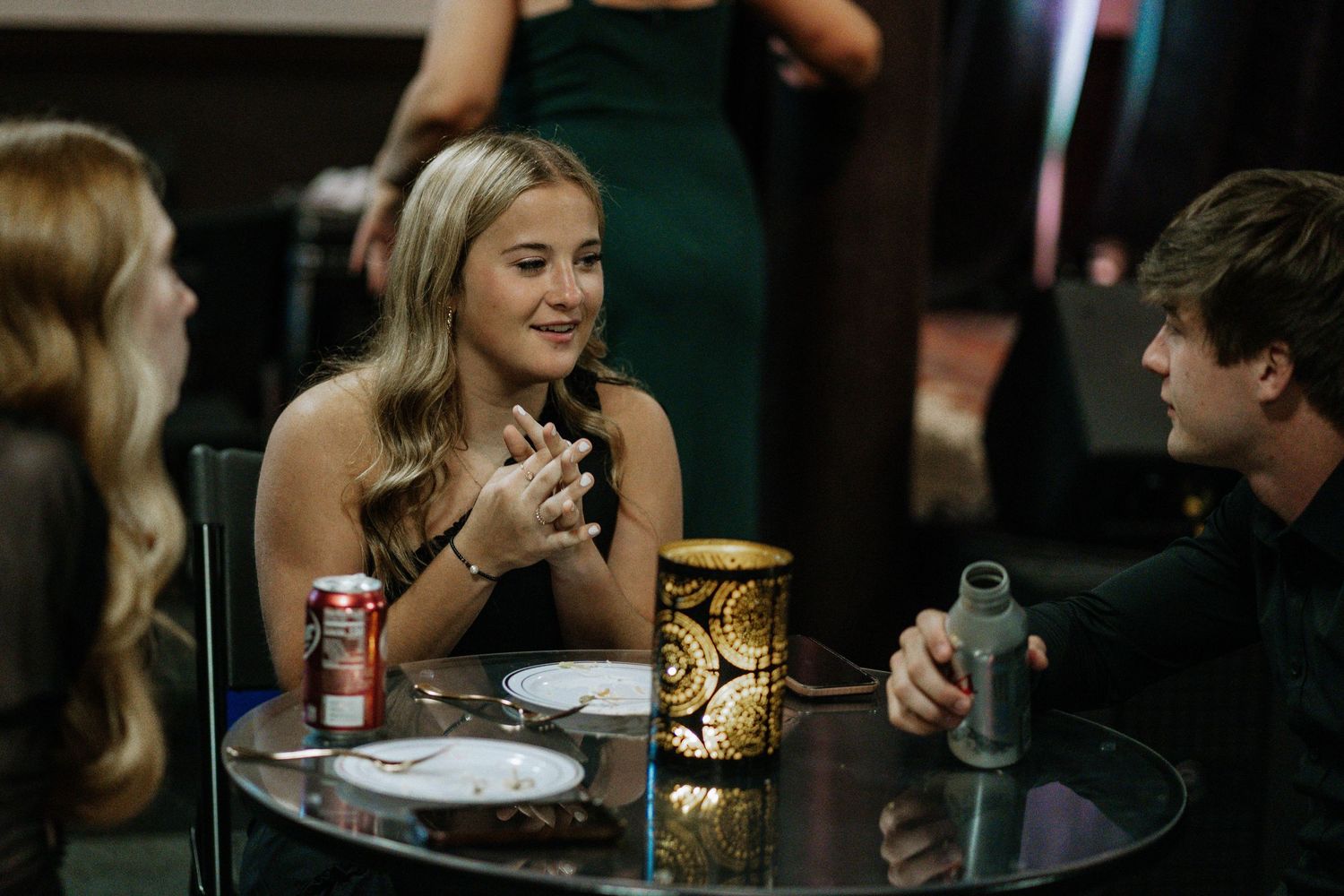Young woman in formal attire smiling at a candlelit table during an elegant evening event.