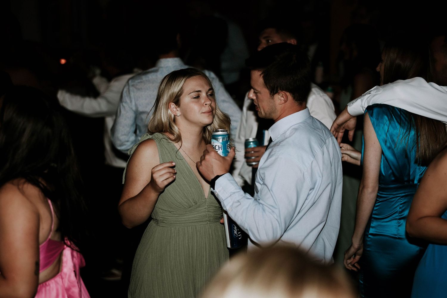 Couple sharing a romantic moment and drinks on a dark wedding reception dance floor.
