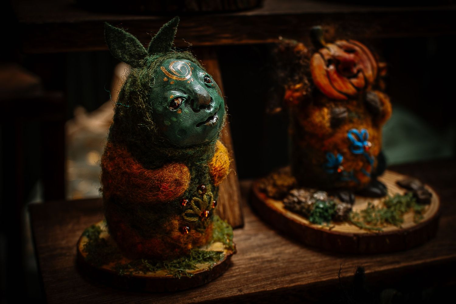 Two whimsical handcrafted fantasy figurines with floral details displayed on a wooden surface in moody lighting.