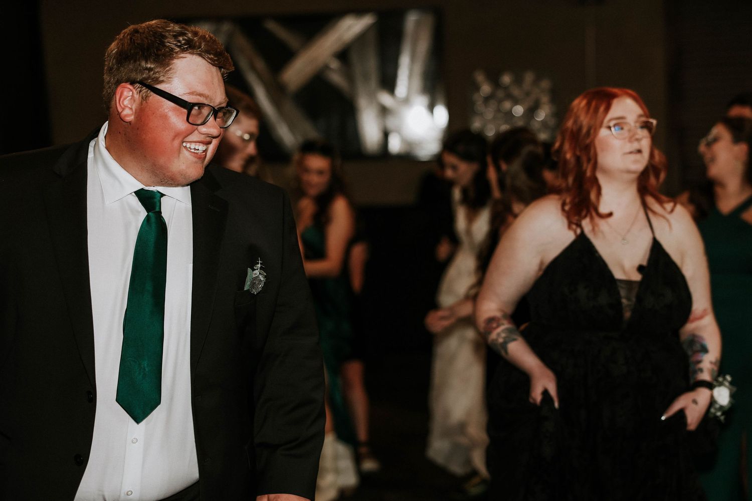 Man in green tie and woman in black dress socializing at a formal event or wedding reception.