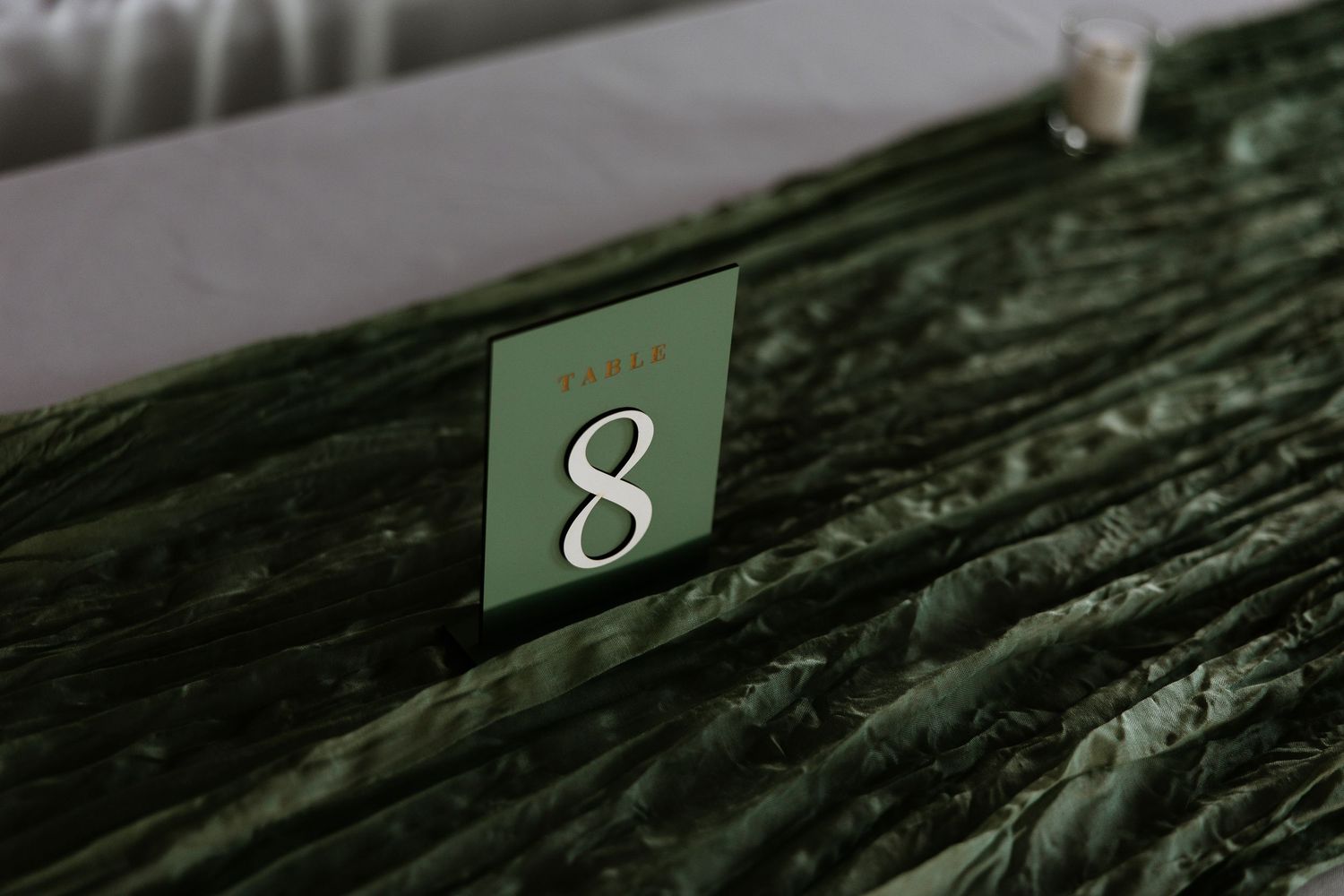 Green velvet table runner with elegant white table number 8 card at a wedding reception.