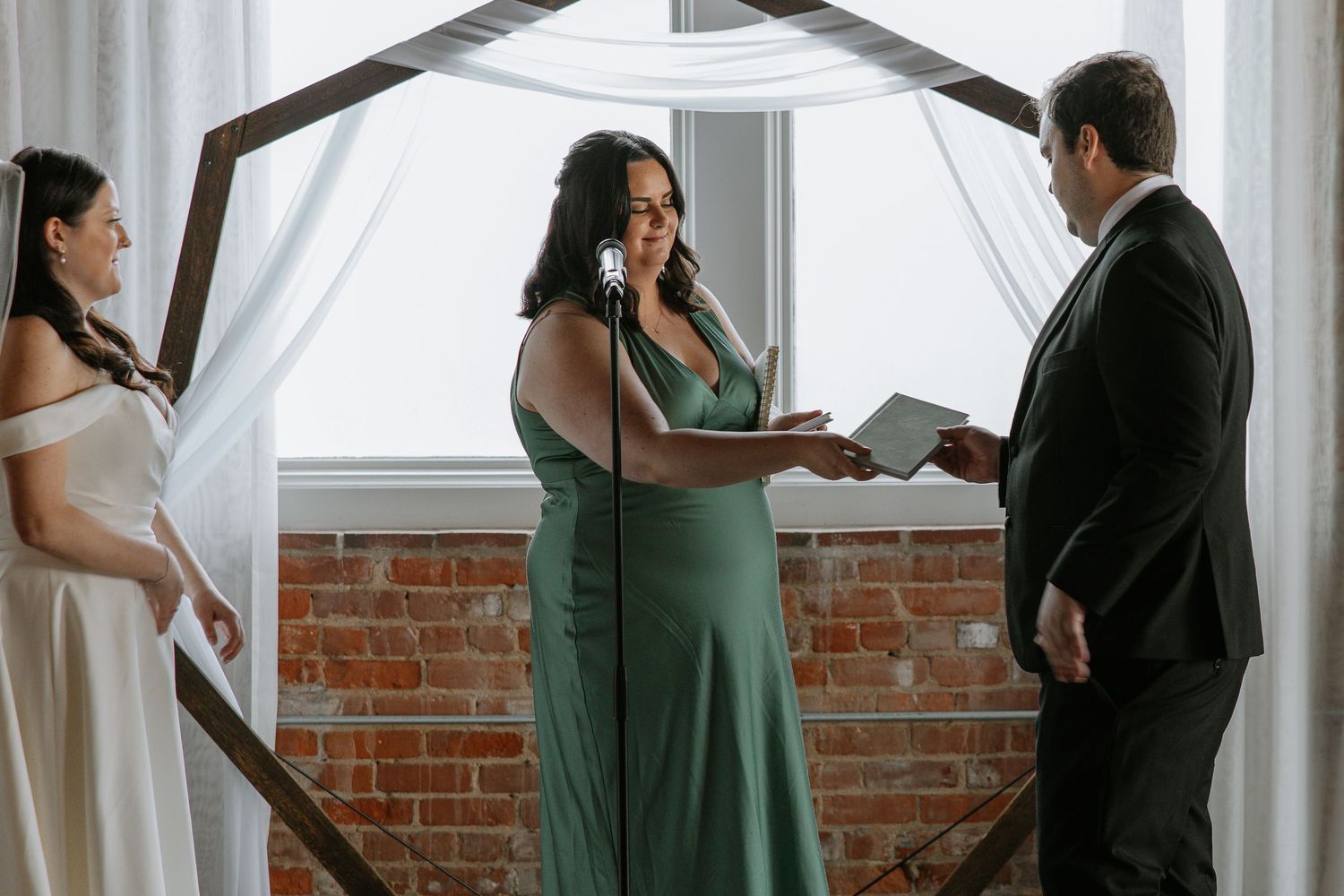 Officiant in green dress reads vows between bride and groom at wedding ceremony.
